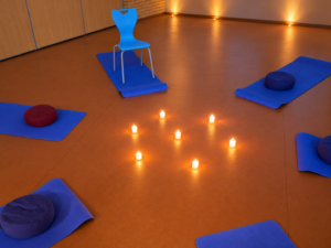 Sfeervolle foto van blauwe yoga matjes in een cirkel met kaarsen in het midden. Illustratie bij thema meditatie-avonden.